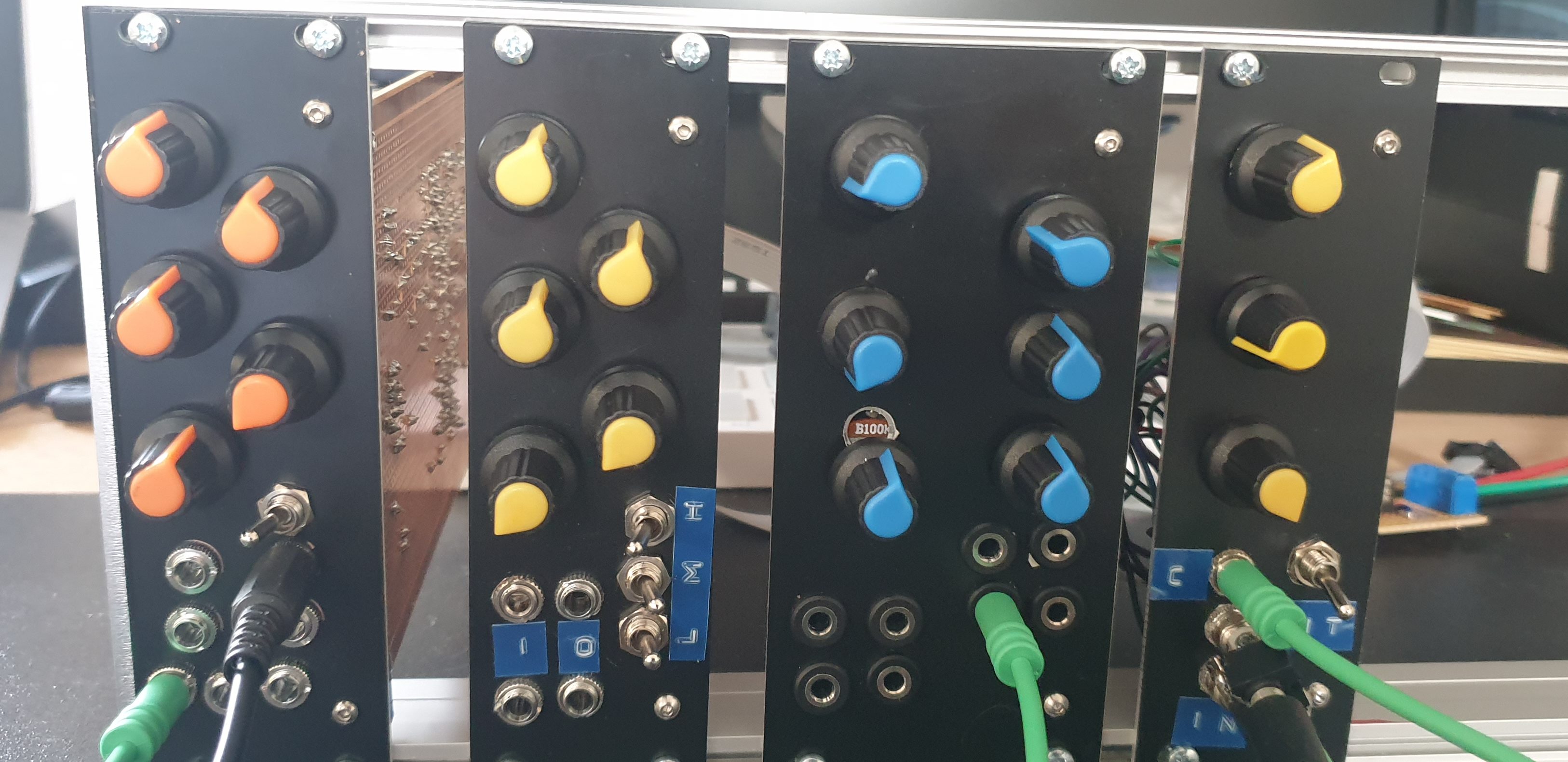 A close-up of a modular synthesizer panel featuring multiple colorful knobs (orange, yellow, and blue) and jacks used for audio connections. The panel is part of a larger electronic setup with visible wires and components in the background.